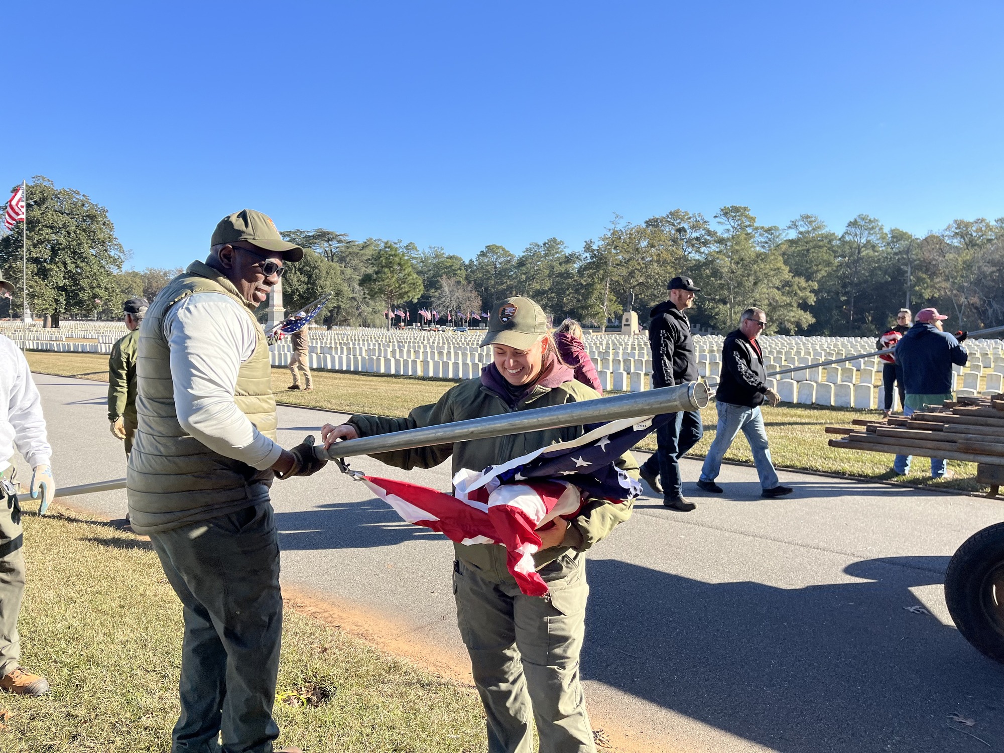 Two people stand among a group of people attaching a flag to the flag pole