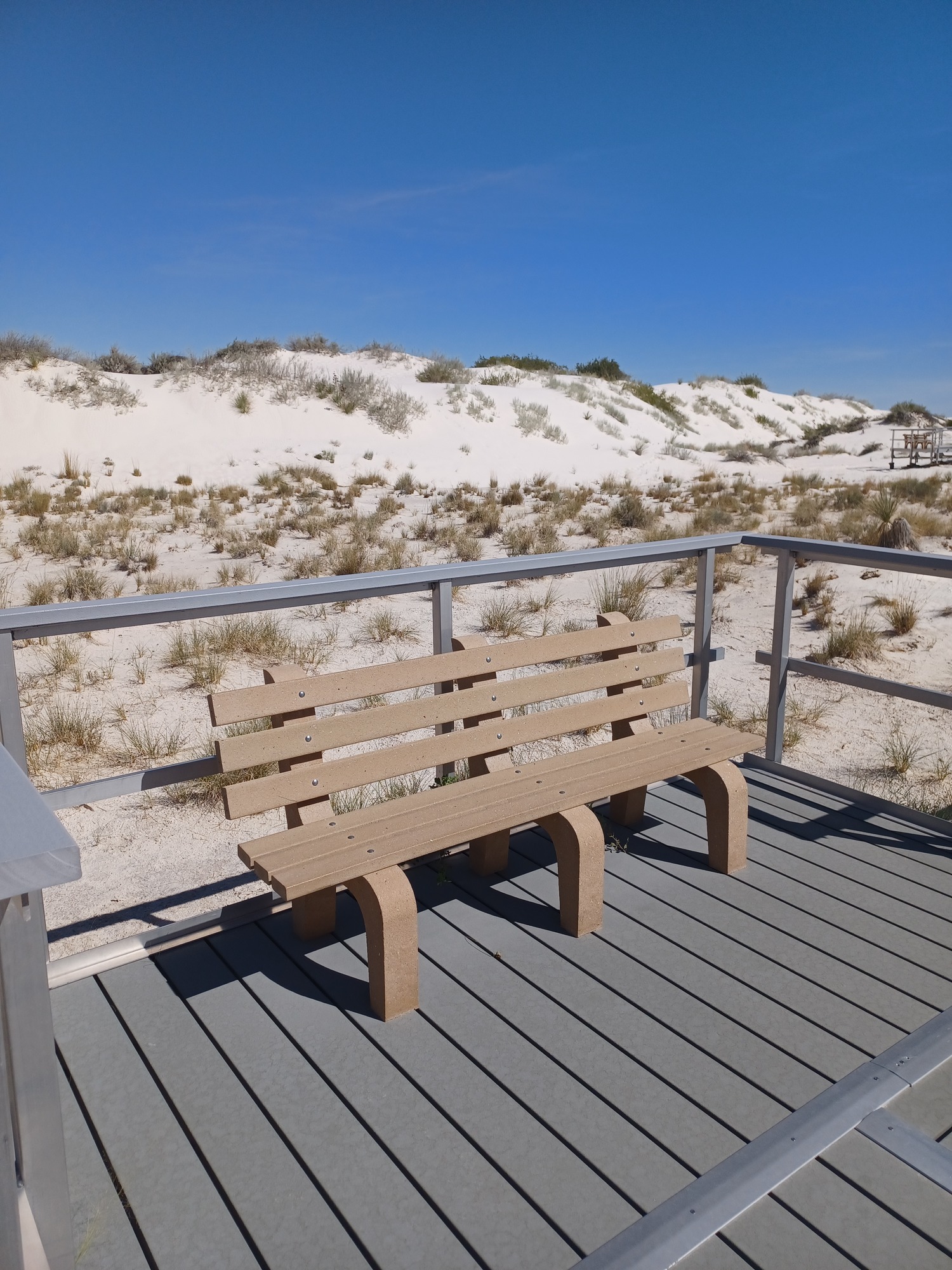 a light brown plastic bench sits on the boardwalk with a white dune seen in the background.