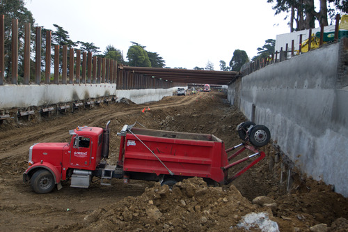 A rocky excavation site with high concrete walls and red dump truck in foreground