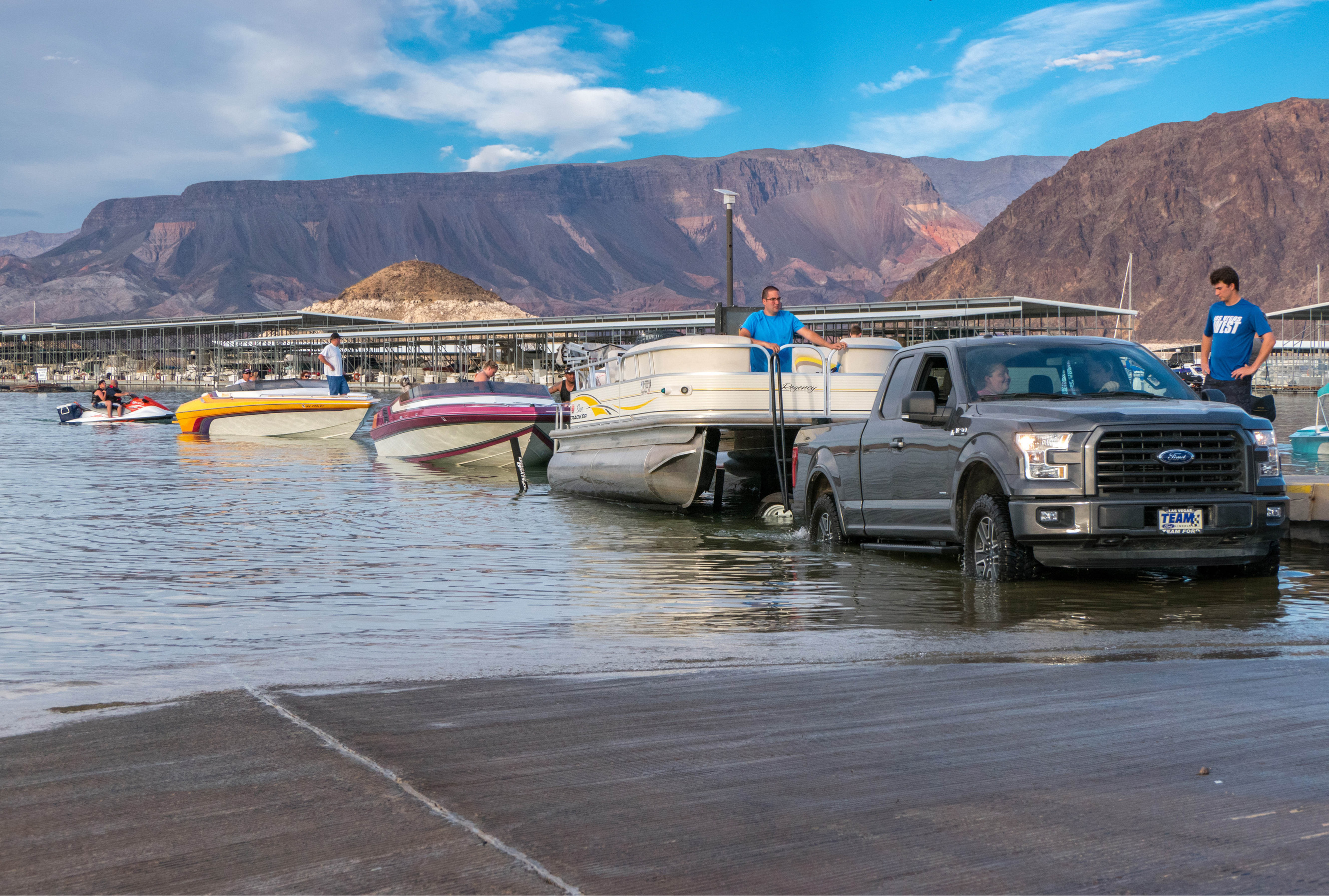Truck and three boats in water, mountains in background