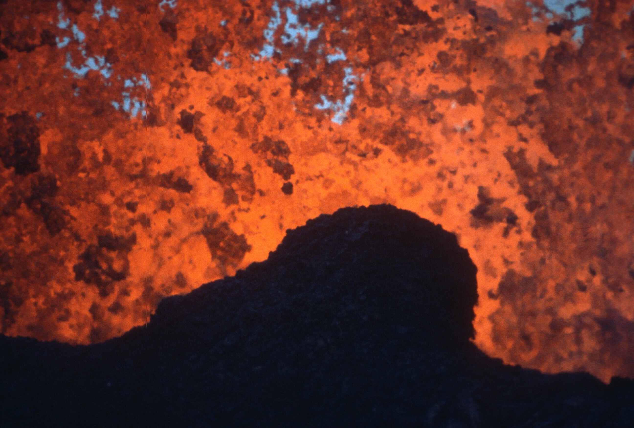 Erupting orange molten lava with a silhouetted rock in the foreground