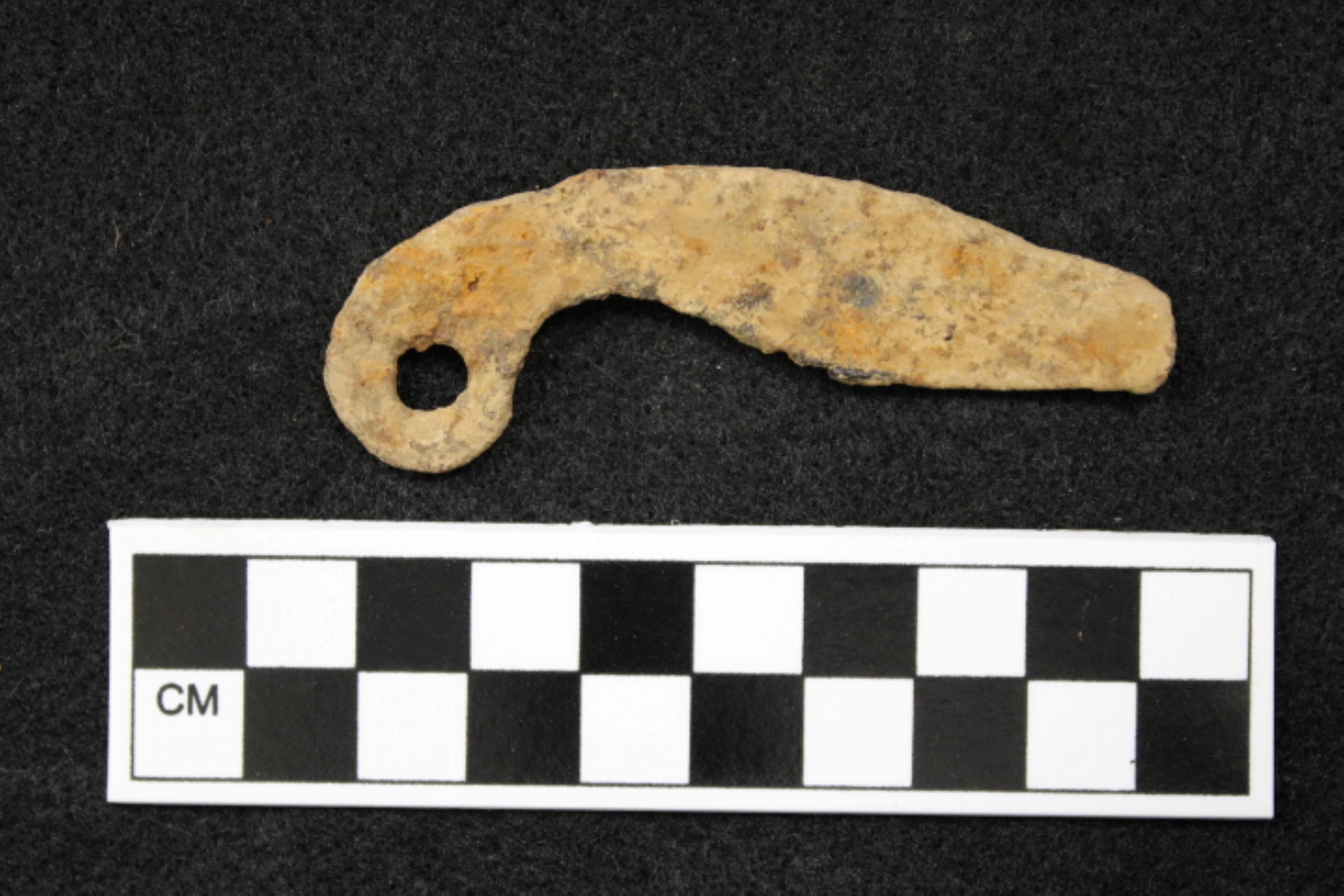 A rusty brown metal items with a hole at one end. Item is curved, 8 cm in length and wide rangers from 2 cm then down to 1 cm and then to 1 1/2 cm.