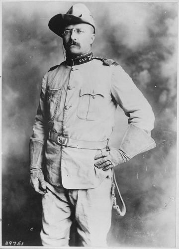 Black and white portrait photograph of Theodore Roosevelt standing, in full Rough Rider U.S.V uniform. 