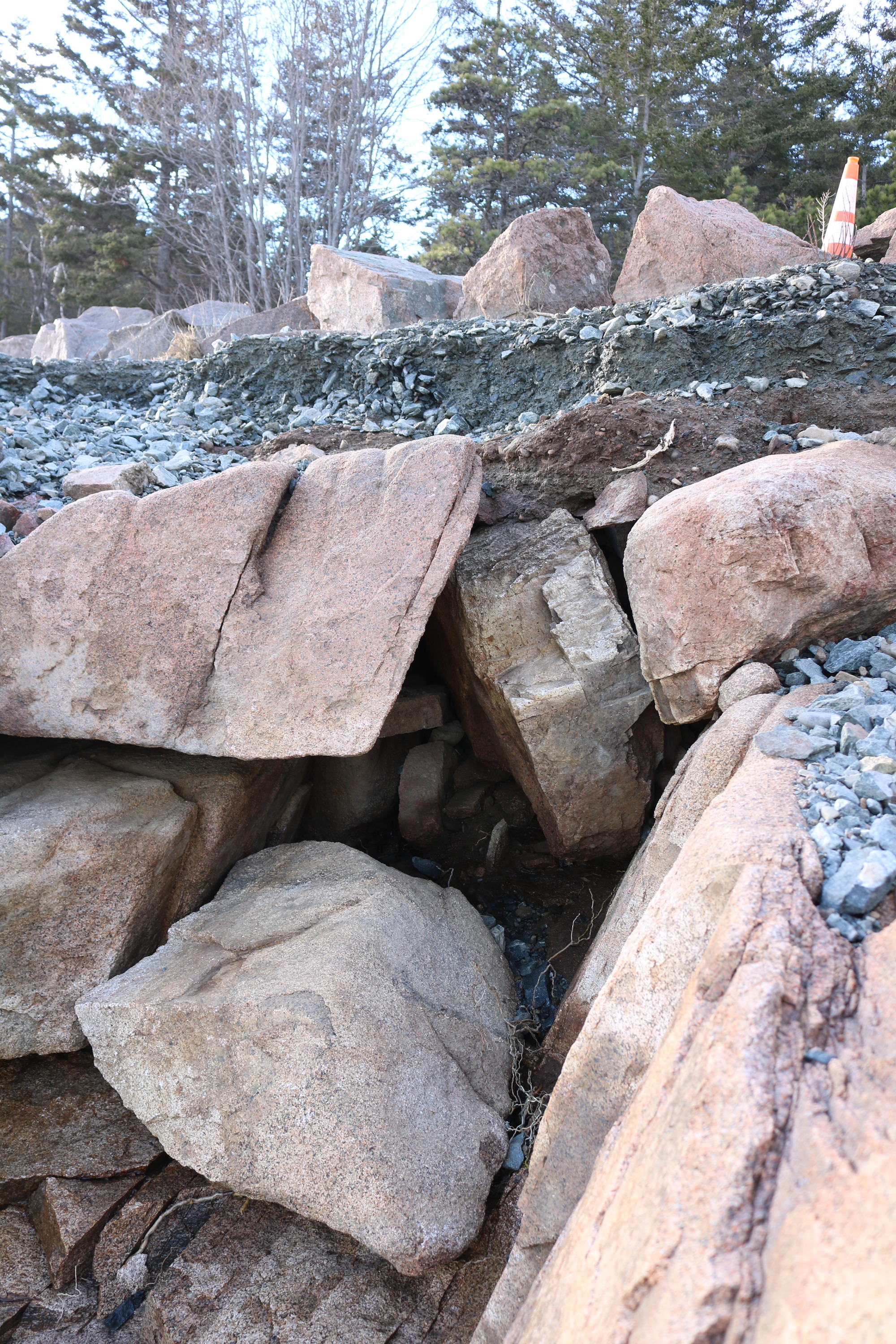 A gravel path is pictured, with significant portions eroded. It is marked with a traffic cone to the upper right. 