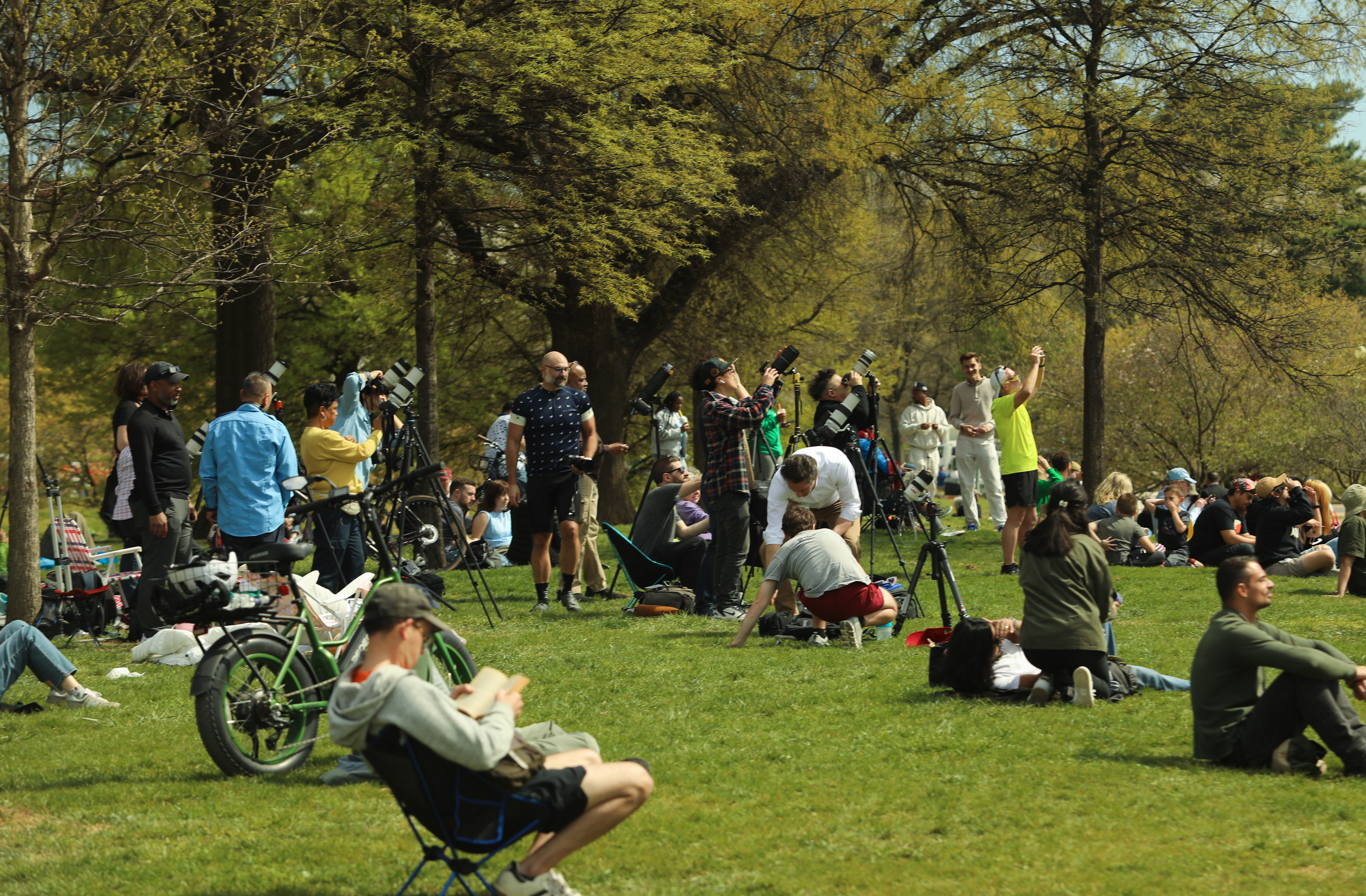 A group of people gather to watch and take photos of the partial eclipse on a large lawn