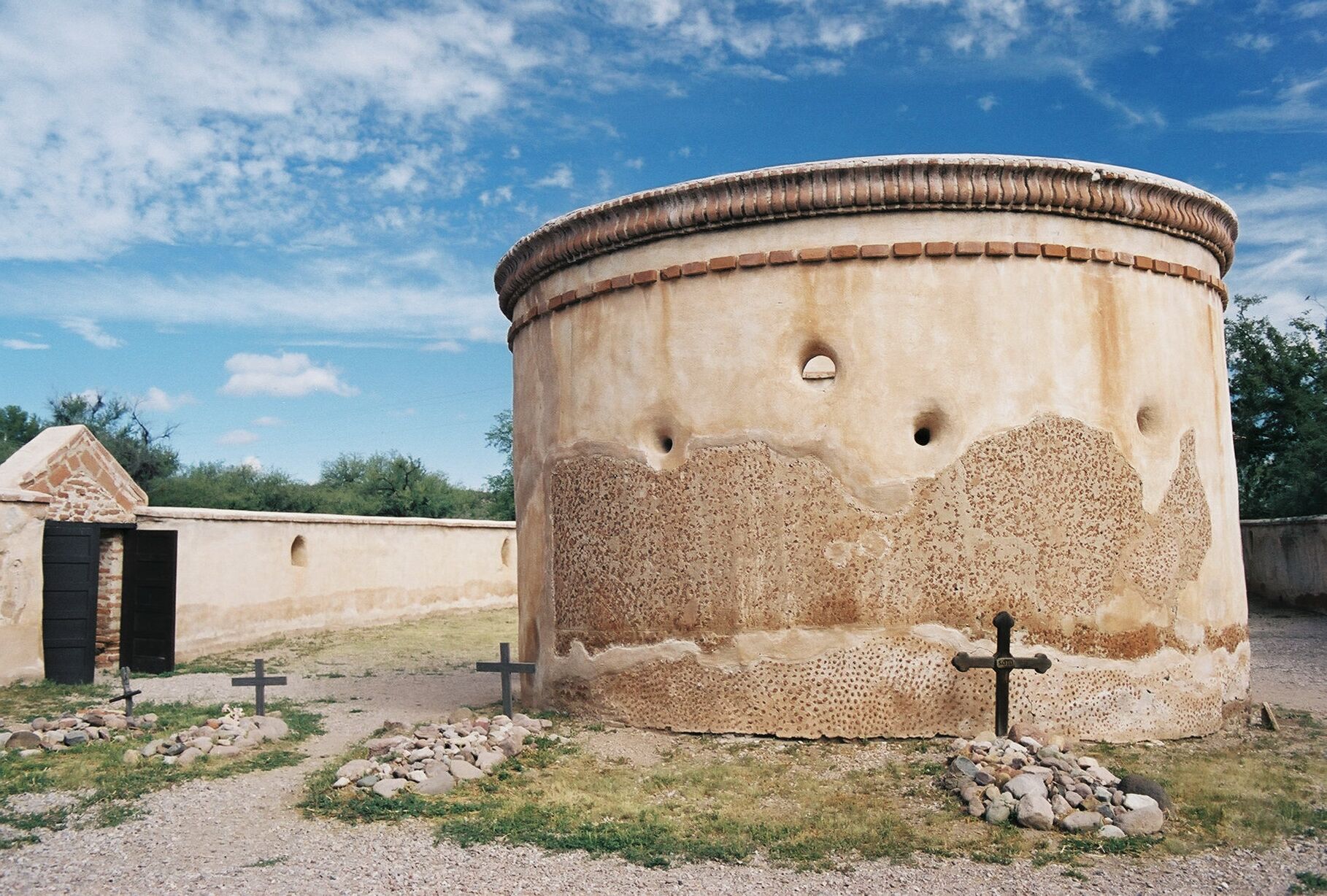 round mortuary chapel with 4 stone-topped gravemarkers, crosses, wall with gate open on west side