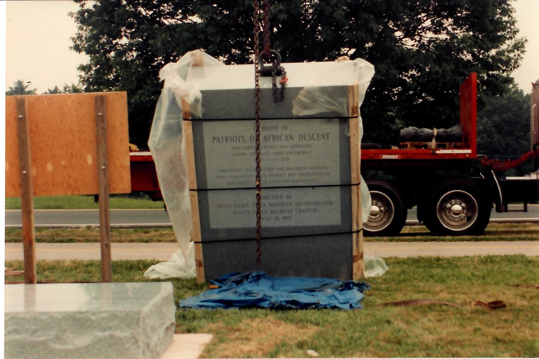 outdoors, crane, flatbed truck, granite block. chain, tarpaulin