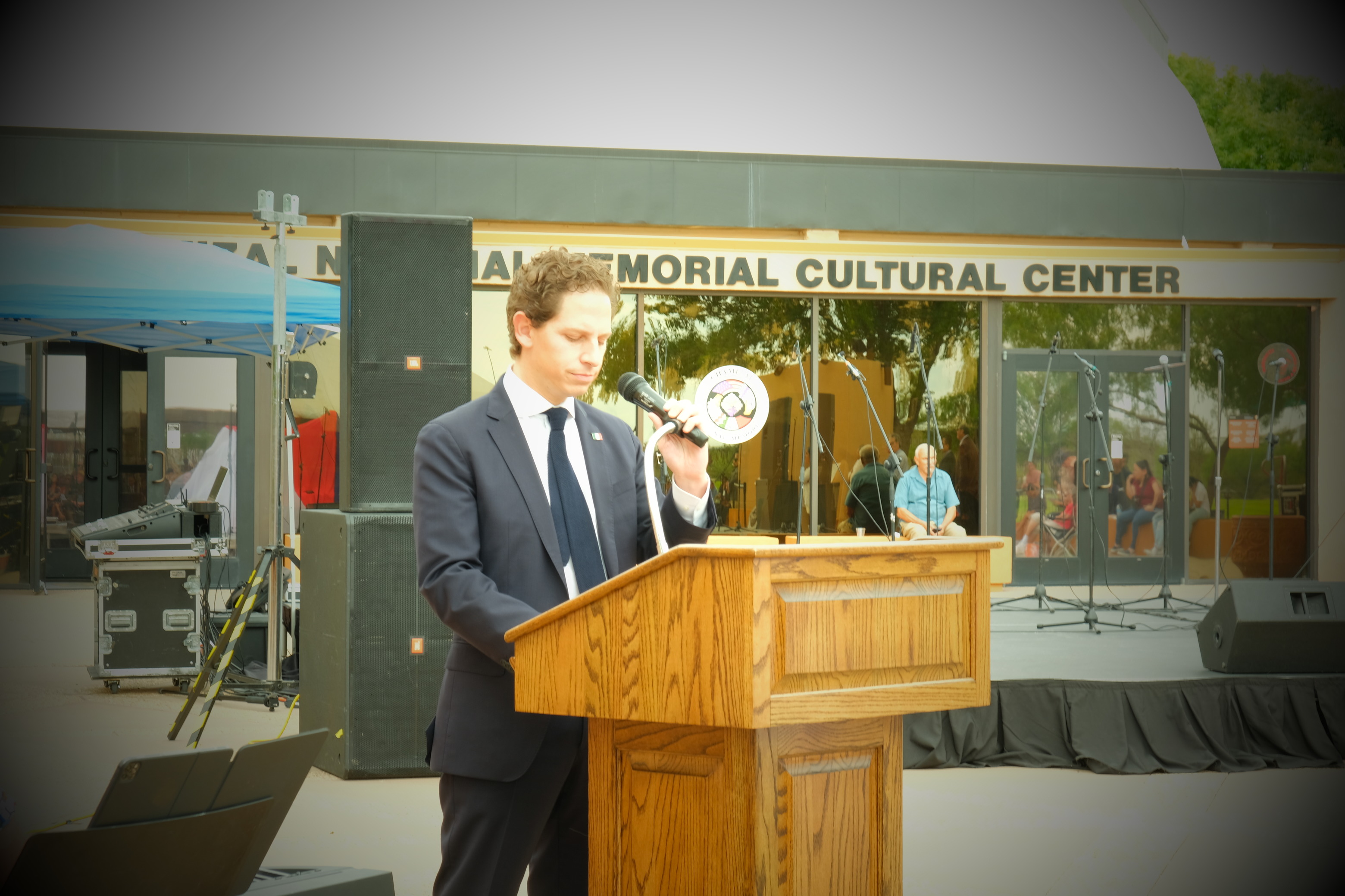 A young man in a dark suit with a Mexican flag pinned to his lapel stands behind a podium