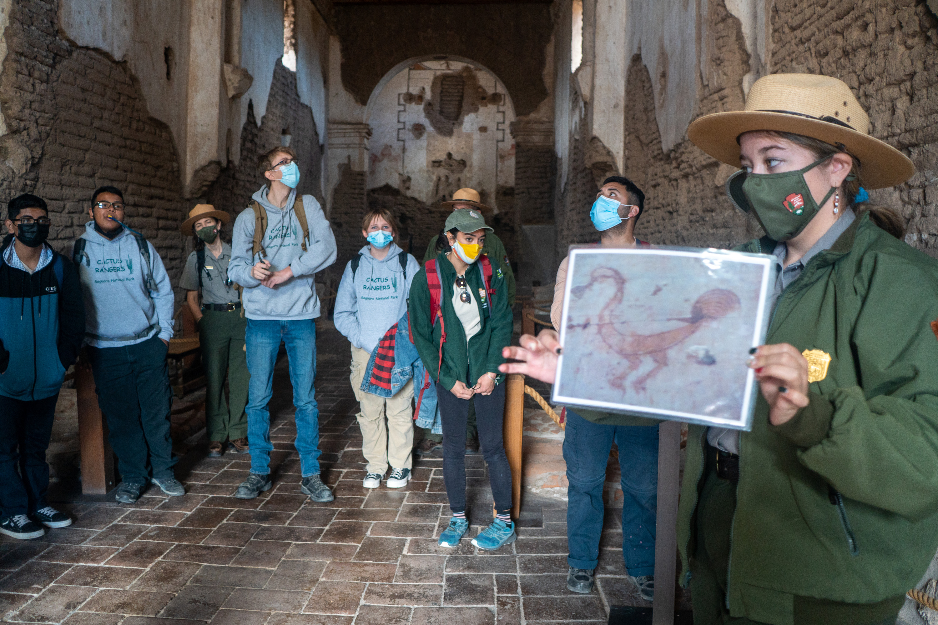 A group of students and a National Park Service employee wear masks inside of an old brick building