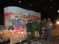 Colorful float with artwork and presents, seven people posing in the snow at night.