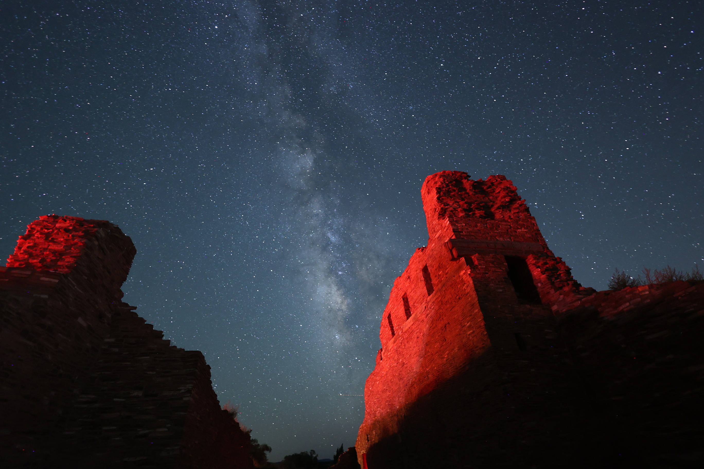 Milky Way in a starry sky with red sandstone church remnants in the foreground.