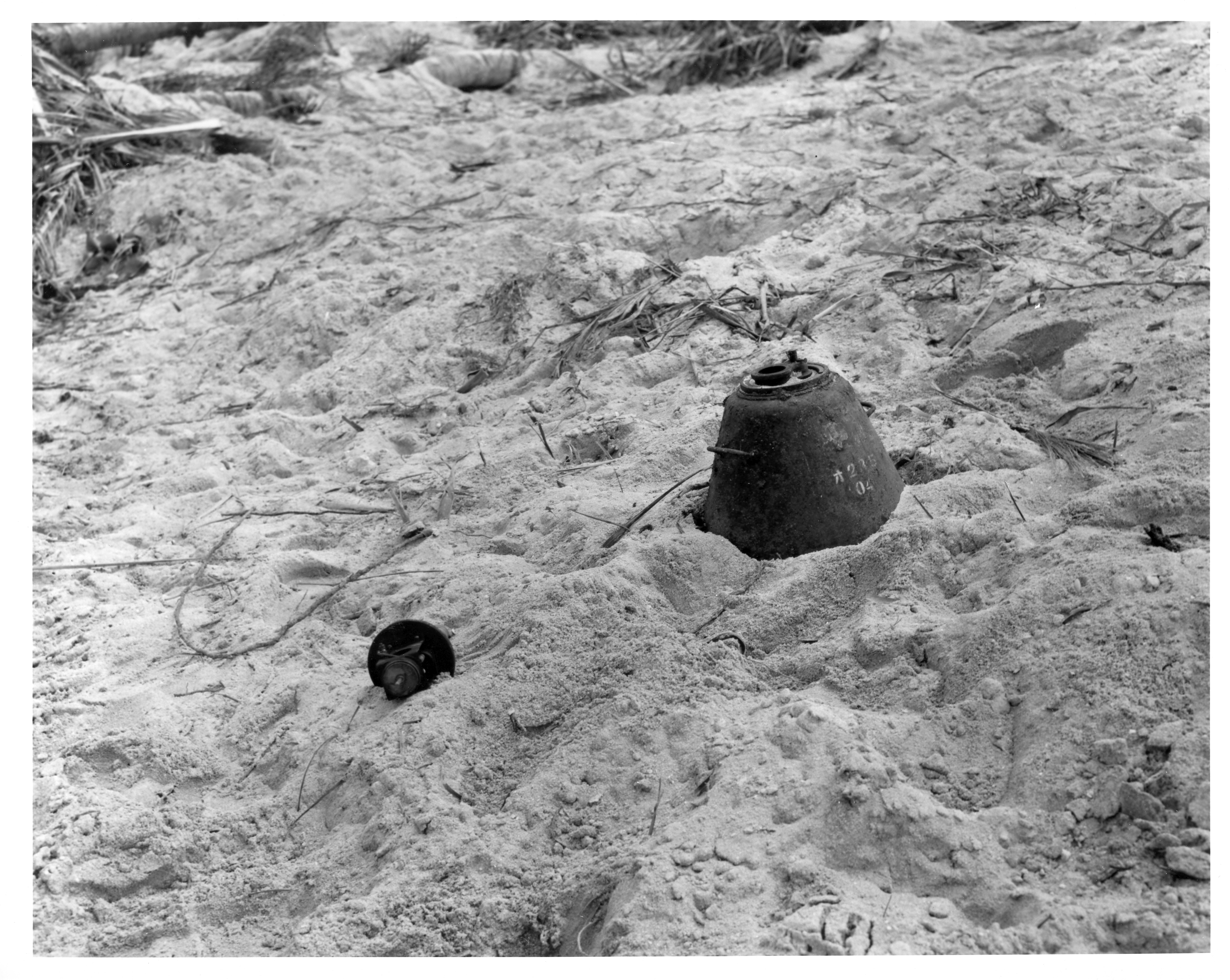 A metal landmine partially buried by sand.