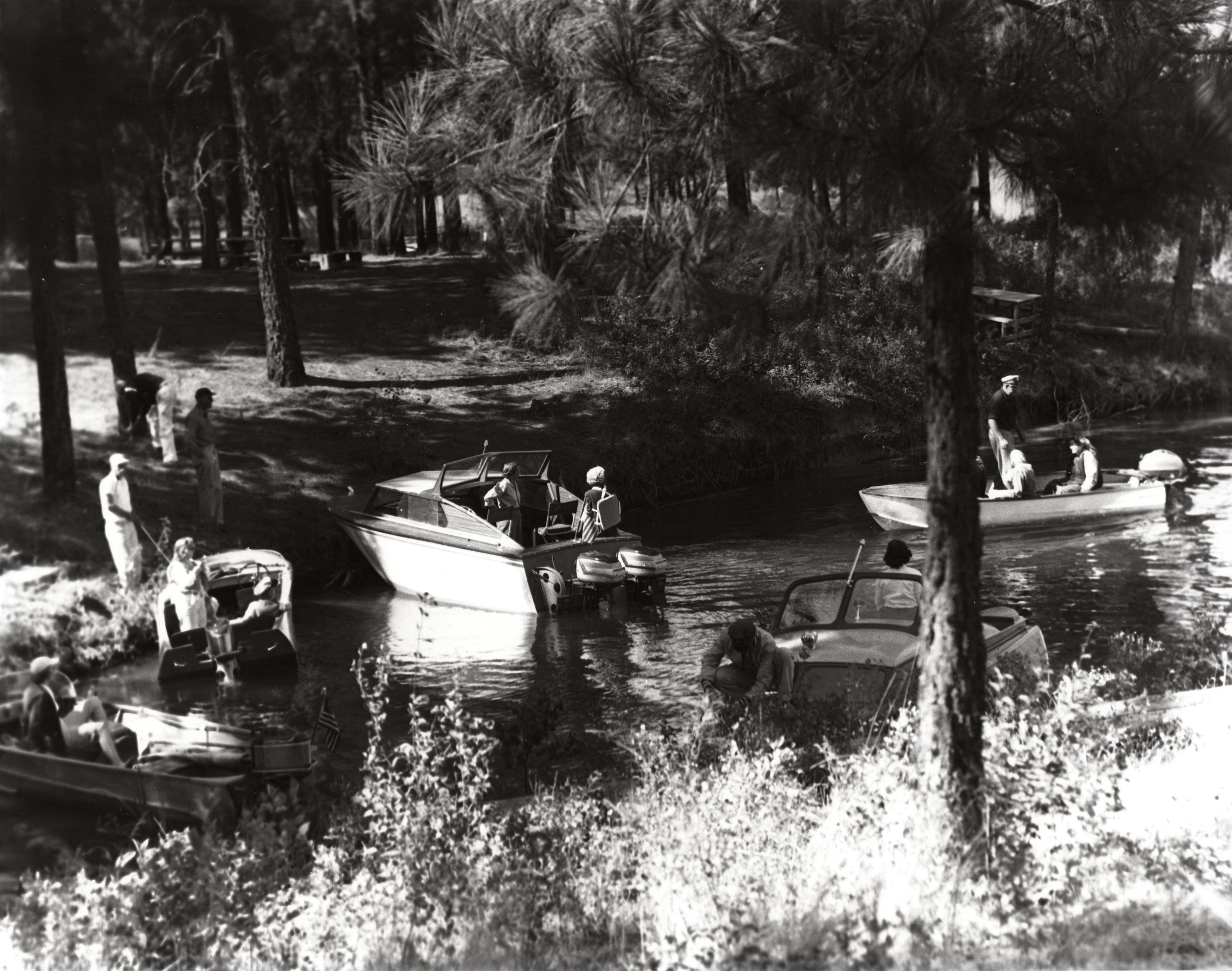 Black and white photograph of five boats moored in a forested cove