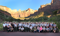 A few dozen rangers pose for a photo in front of a red and orange mountain.
