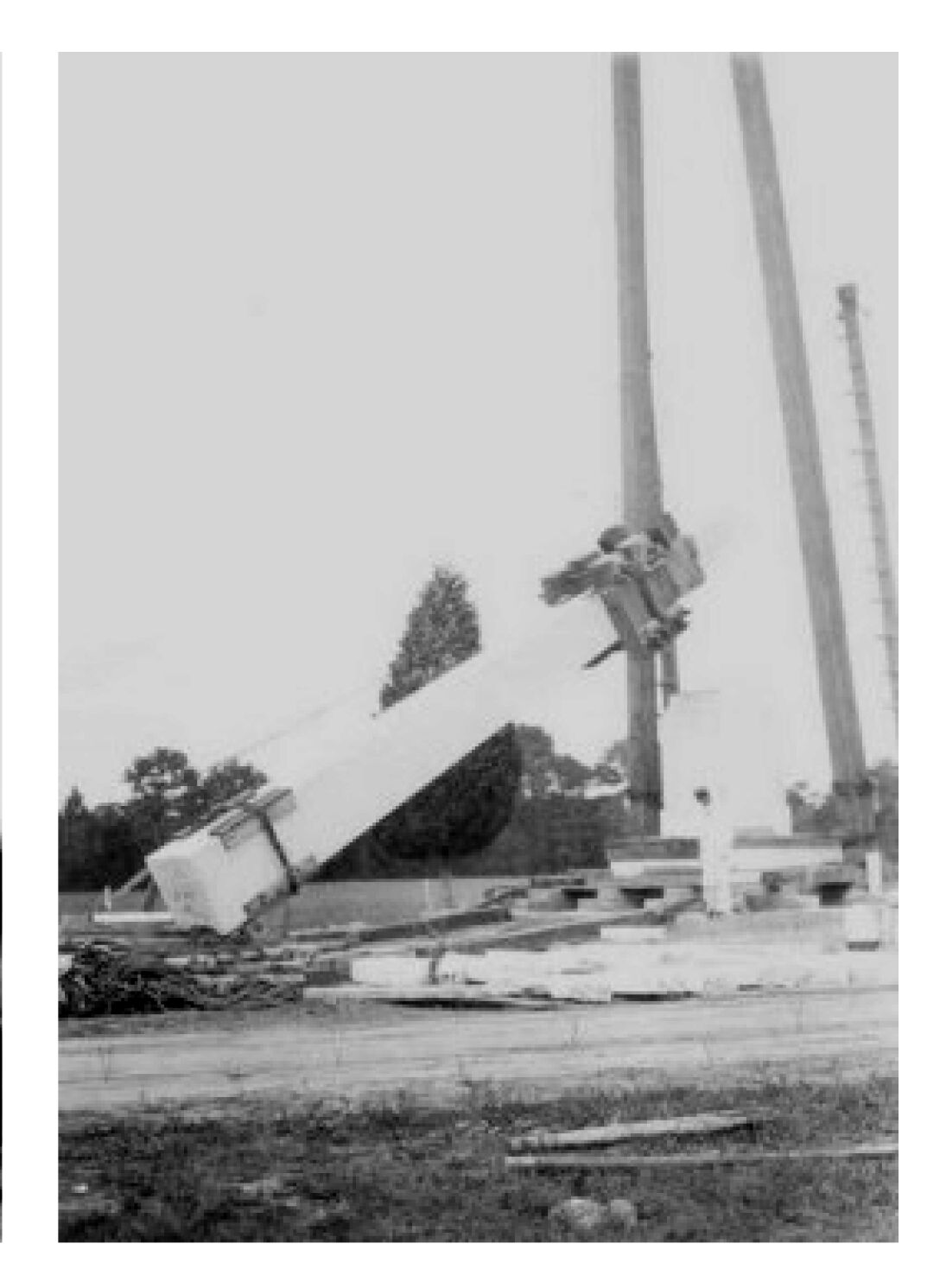 White obelisk with base on logs and top in the air attached to the derrick