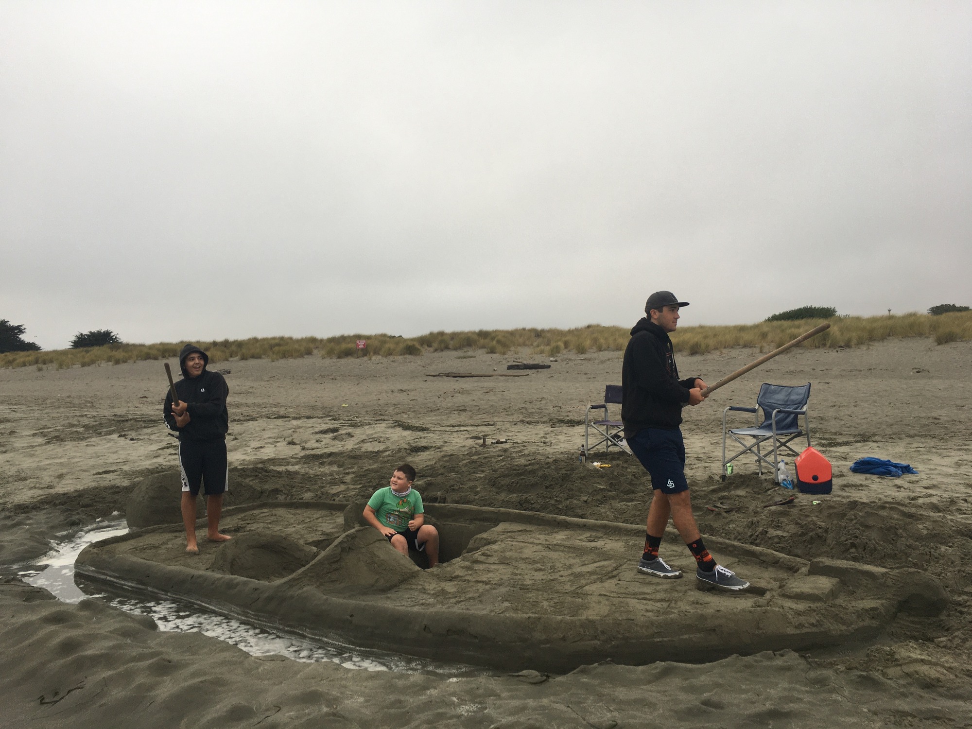 A 22-foot-long, nine-foot-wide sand sculpture of motorboat. The gunnels of the boat are only about a foot above a moat of water. A cockpit and passenger seat have been carved into the stern end of the boat. A young boy sits in the passenger seat as two older males stand on the boat's decks pretending they are fishing.
