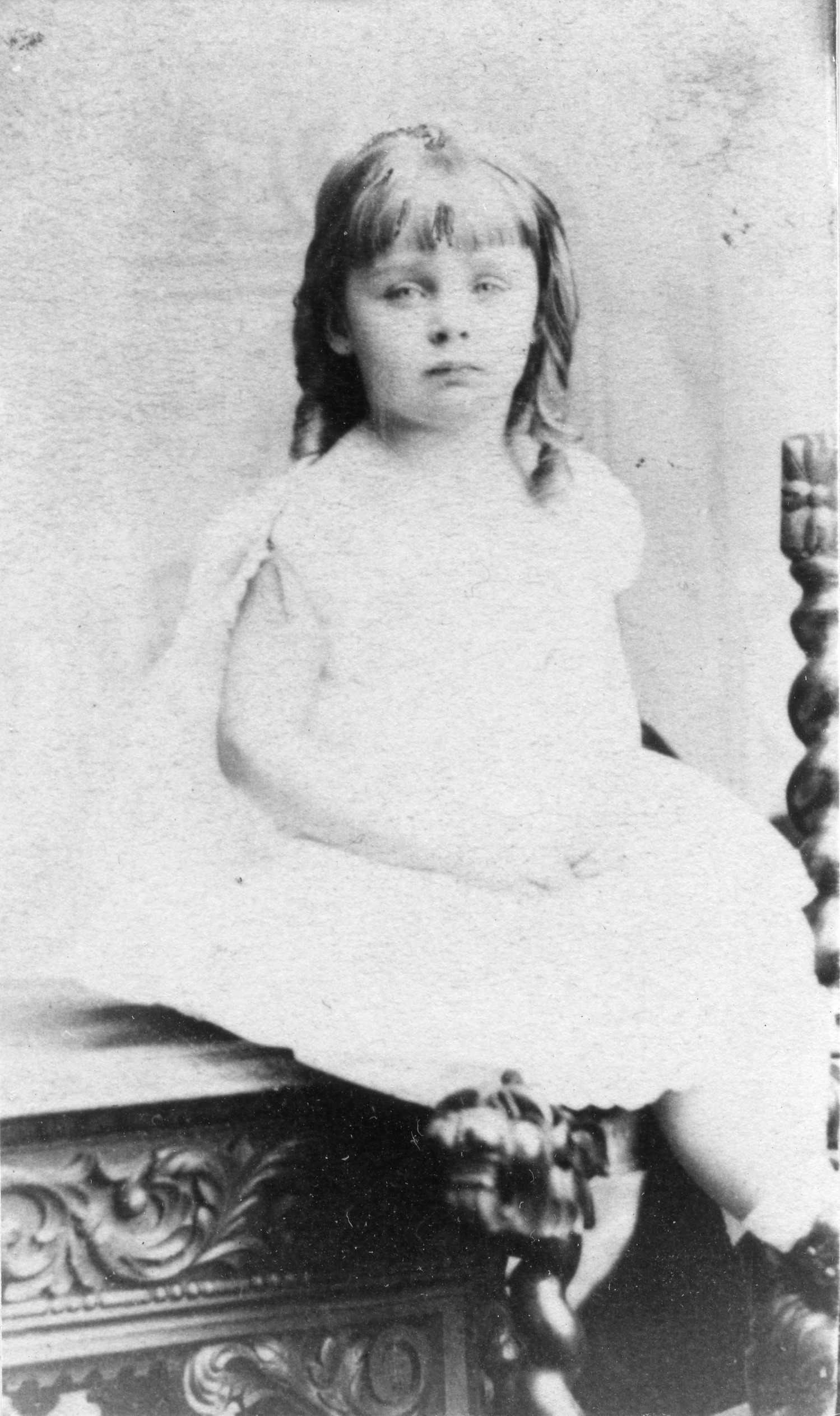 Three quarter length photo of a young girl sitting and wearing a dress.
