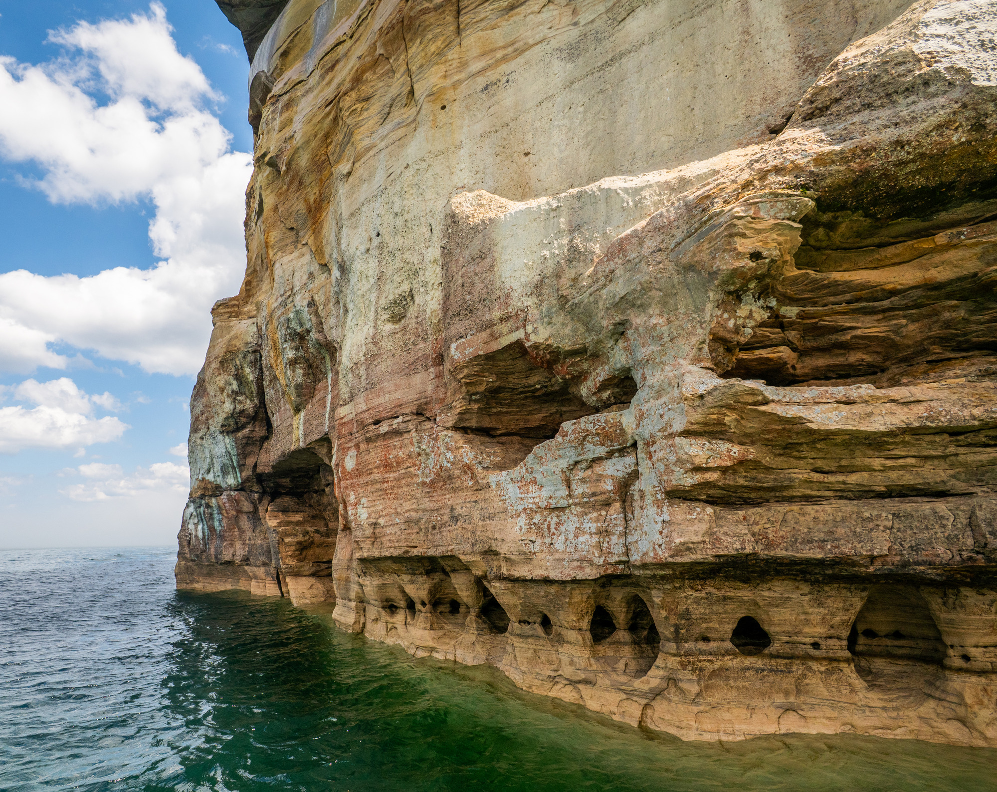 Mineral-stained cliffs with lots of small caves and columns at the base rise out of Lake Superior