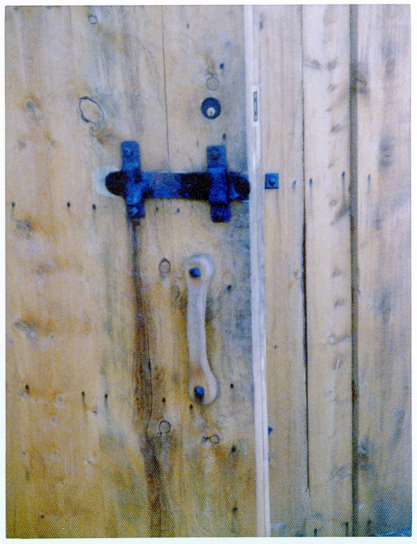View of a wooden door handle and metal clasp on the door to the administrative office area. A modern circular metal keyhole is visible above the forged metal apparatus. 