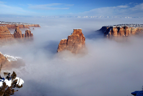 large sandstone rock spire and vertical cliffs peeking above dense white clouds and snow