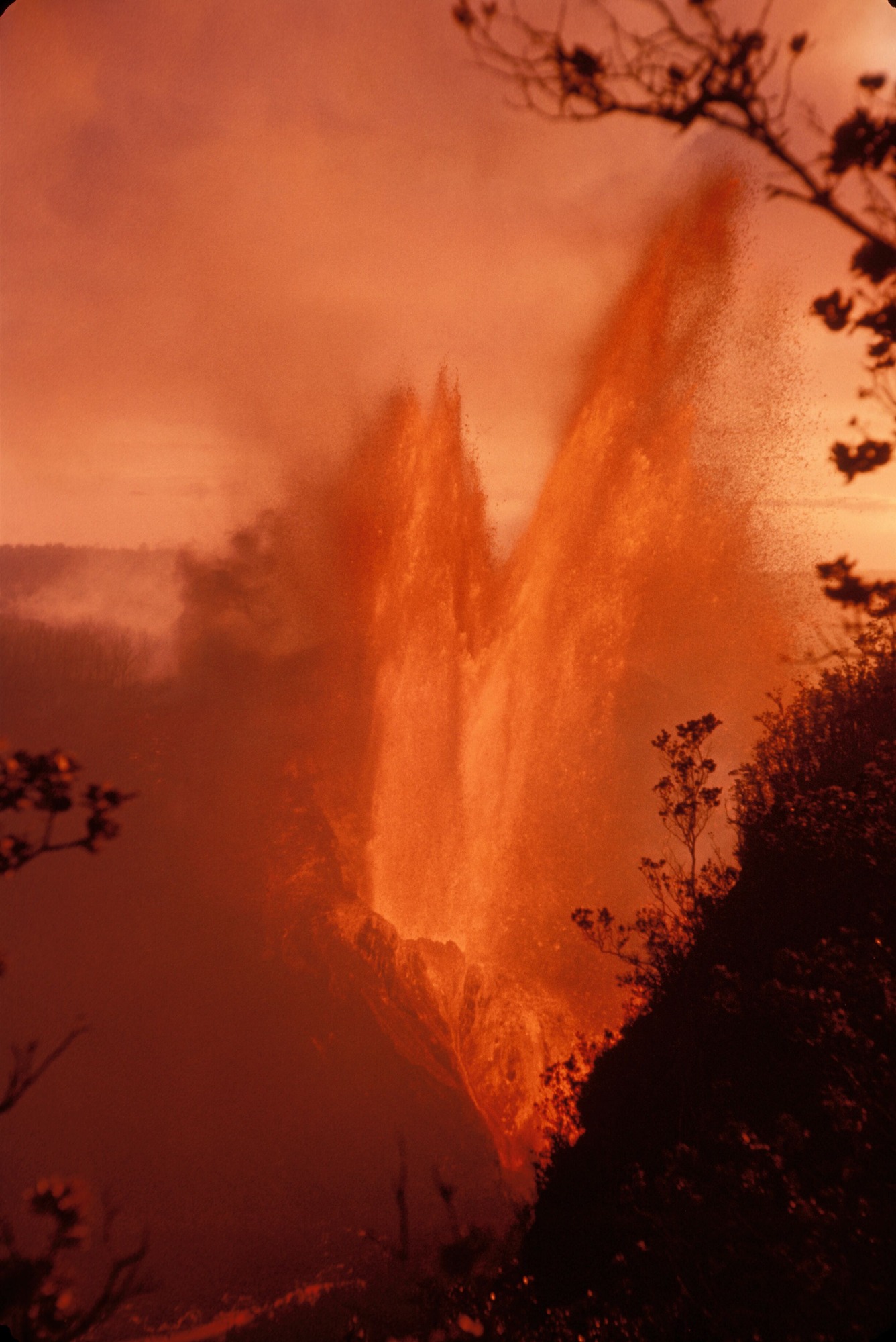 Tall lava fountain erupting from the steep, vegetated walls of a crater