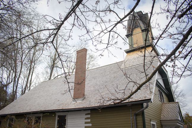 The church stands behind a tree; plywood covers the holes in the steeple, and recent work on the chimney is clear from an unpainted section of siding.