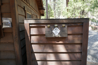 A wooden box sits next to a wooden building. A metal hinged door opens into the box. 