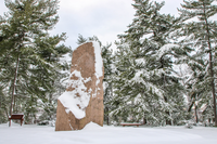 Granite monolith on a plaza surrounded by trees after a snowfall
