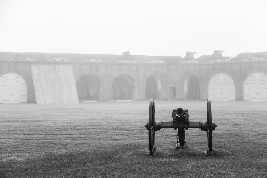 A cannon sits in the center of a foggy parade ground of a fort. 