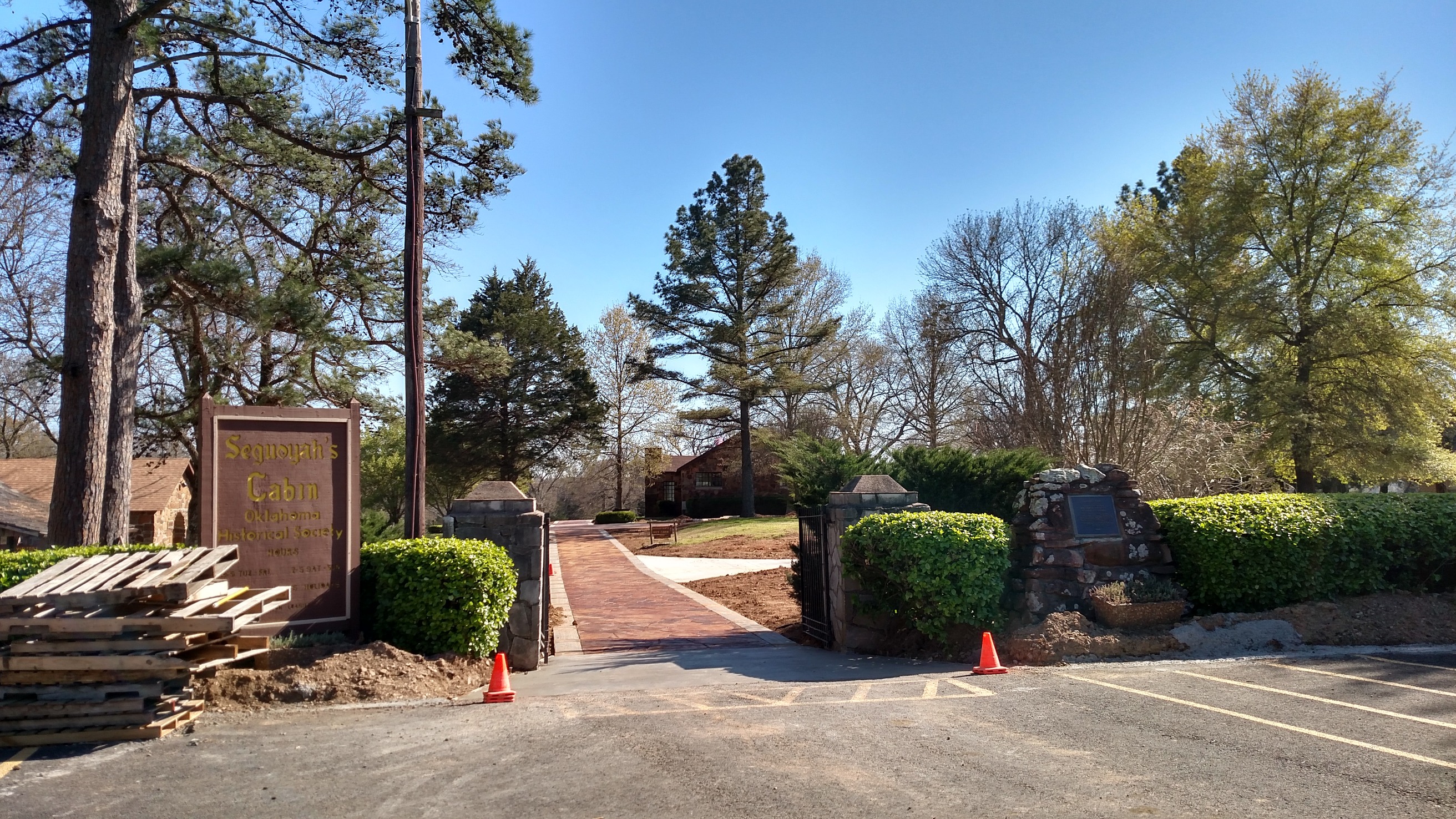 A park entrance with a stone and wood sign, green shrubs, and tall trees against a clear blue sky.