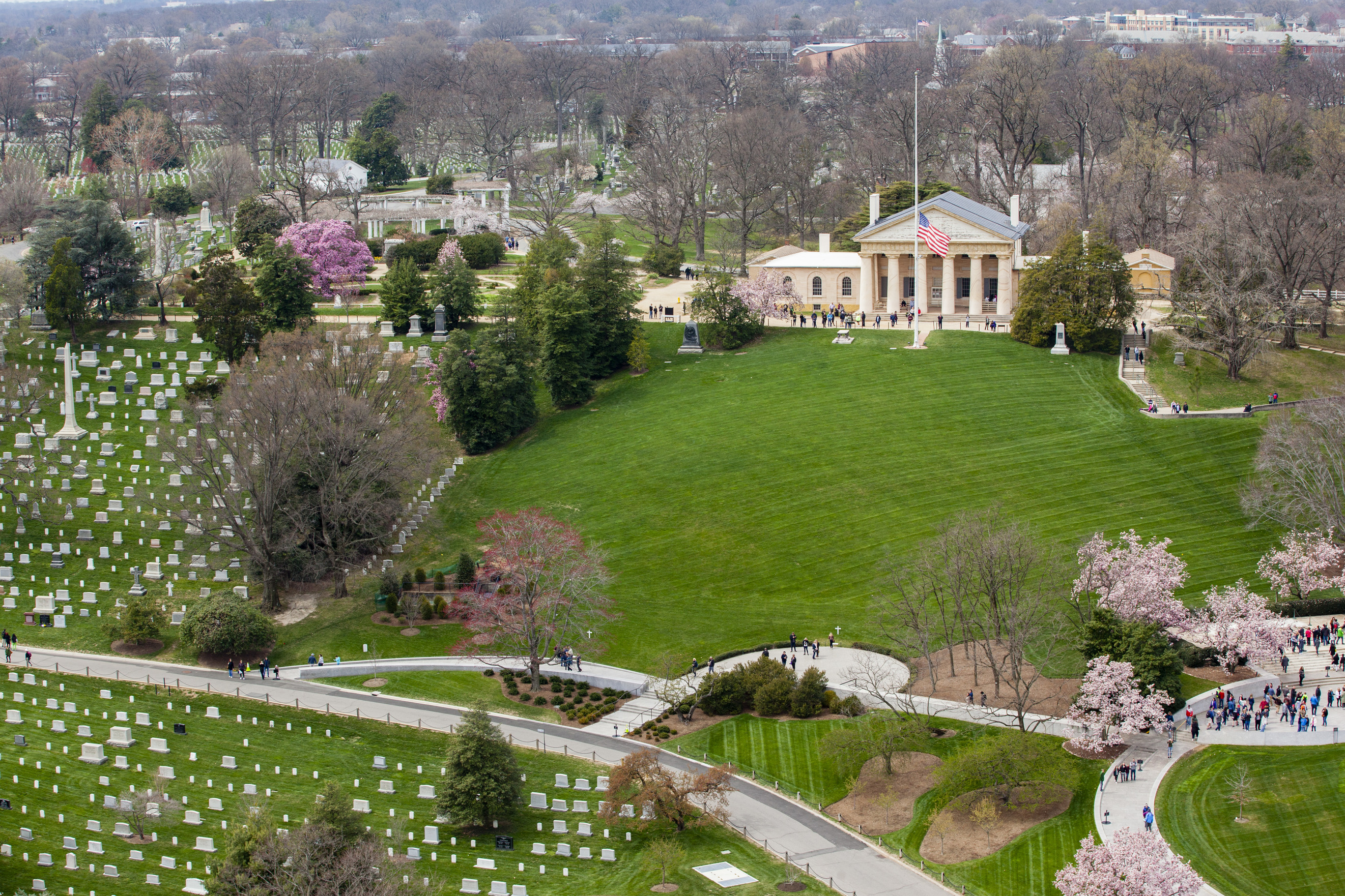 An aerial view of Arlington House in the spring time. Cherry blossom trees are in bloom and the flag is at half mass.