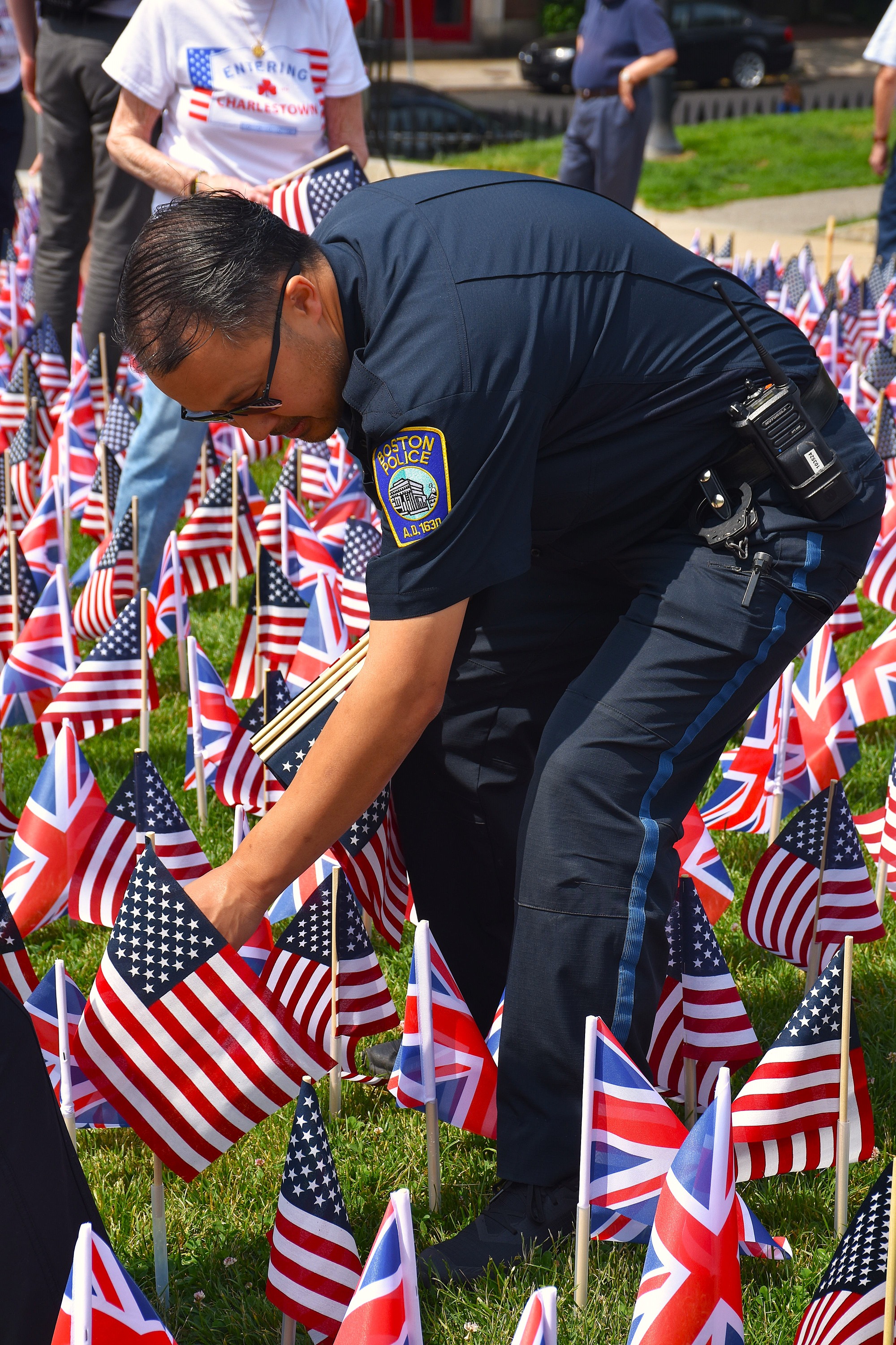 A uniformed Boston police officer plants a US flag amidst rows of small US and British flags.