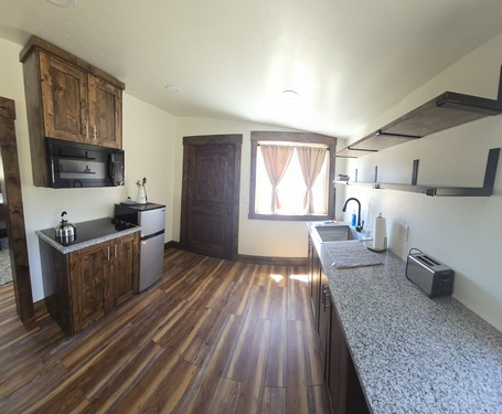 The bunkhouse has a rustic aesthetic with wood wall and ceiling paneling, a wood burning fireplace, kitchenette, and dining area.