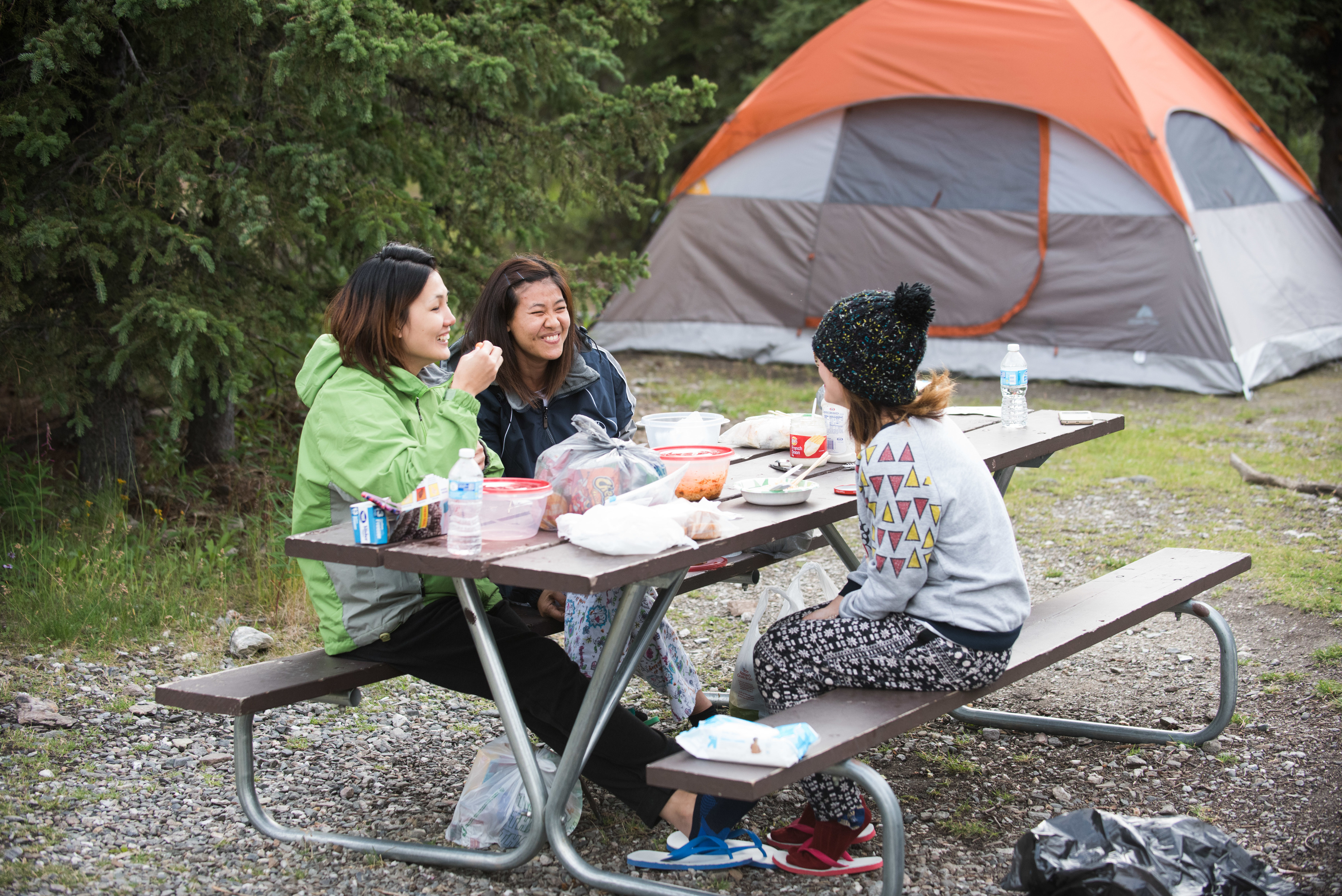 three women eating at a picnic table near a tent