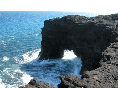 a rock wall with a hole in the bottom juts out into the sea