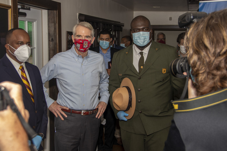 A man in a blue shirt and red mask stands next to a park ranger holding a flat hat.