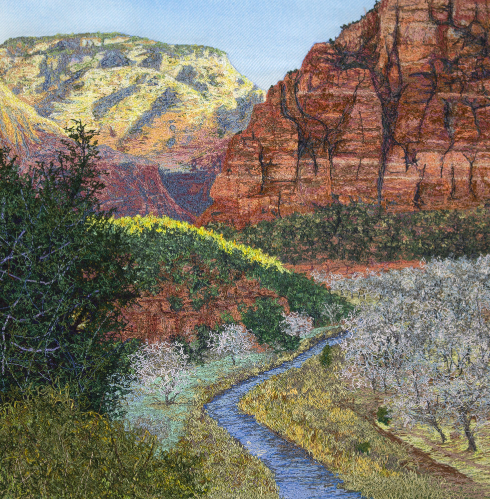 An image created using colored thread on fabric. A blue river flows down from a sandstone canyon. Along the river, various cliffs, shrubs, trees, and grasses are visible. In the background, massive sandstone formations stand above the canyon. The stone is a variety of colors, including white, yellow, orange, red, brown, and some purple.