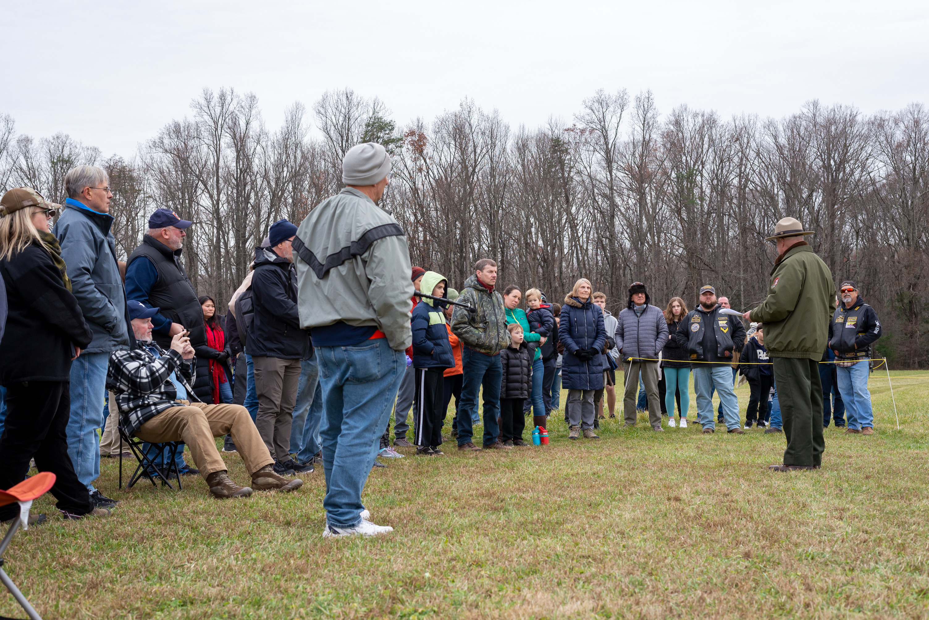 A park ranger stands in a field speaking to a crowd of 75 visitors.