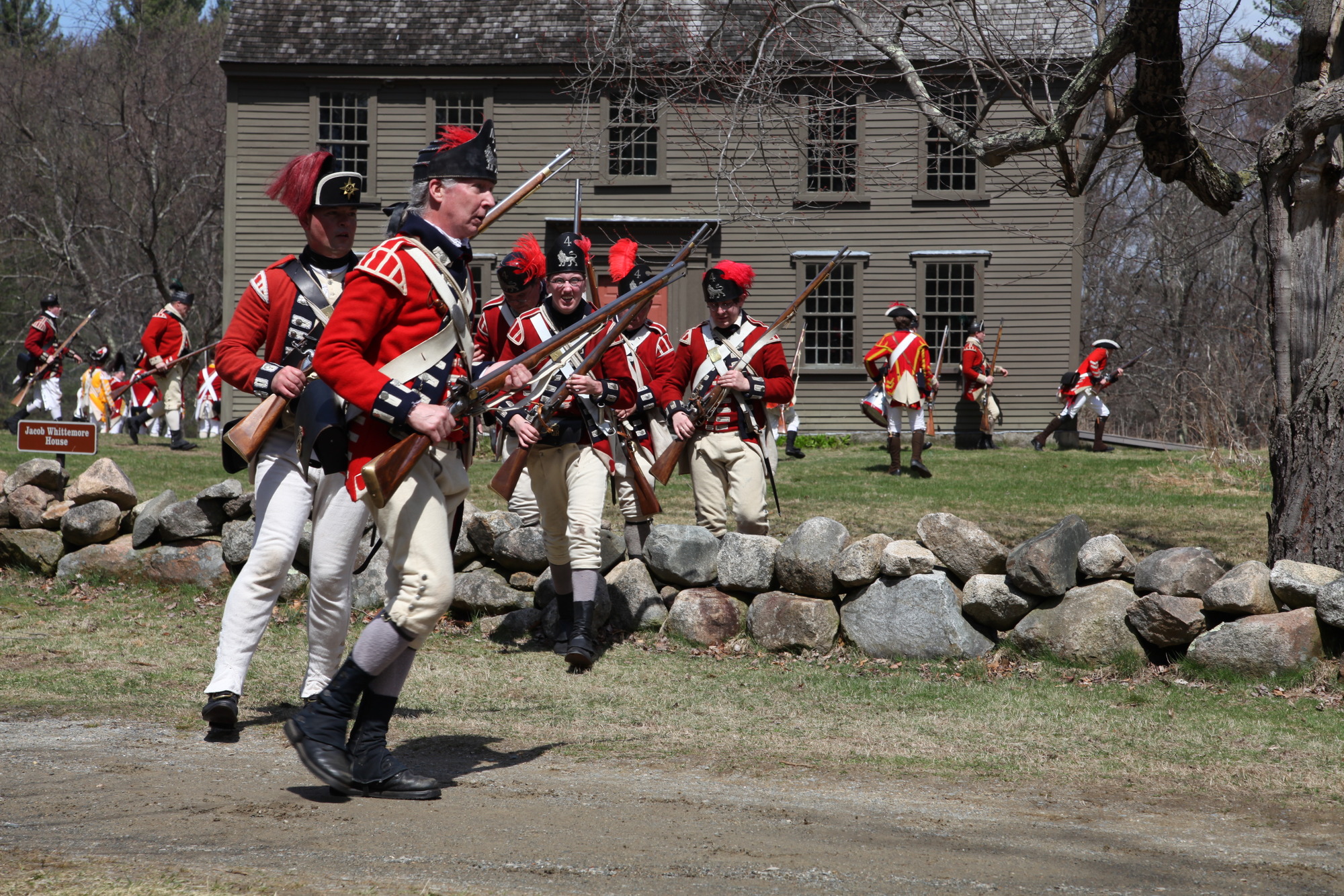 Several men dressed as British solders during the Revolution surround a historic building