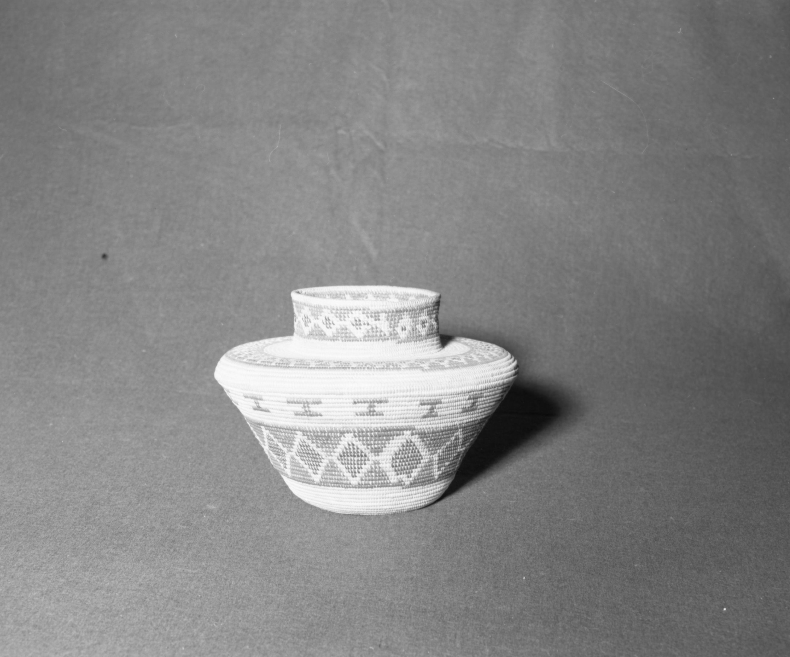 Mrs. Donald Segerstrom Collection. Object: Yokuts basket. Dimensions: 10 x 8". Materials: Grass bundle foundation, bracken fern, sedge root, redbud. Technology: Non-interlocking stitch, rightward coil direction, fag ends trimmed on work face, moving ends trimmed on interior. Photographed by Michael Dixon. Catalogued by Craig Bates and Barbara Beroza. Yosemite Collections, National Park Service. 1/83.