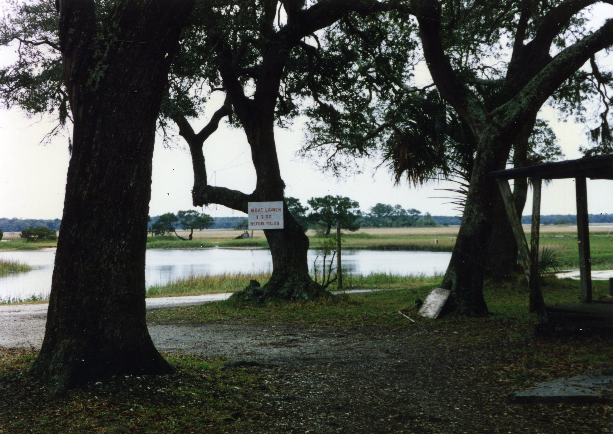 a grainy color photo of a sign that read boat launch $2.00 an a creek with marsh