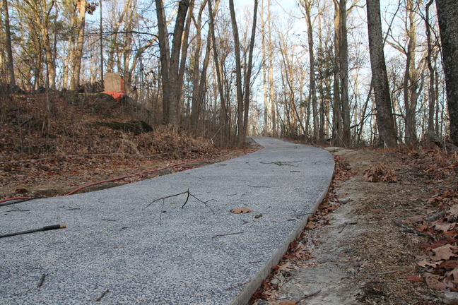 A concrete path winding to the left into a wooded area.