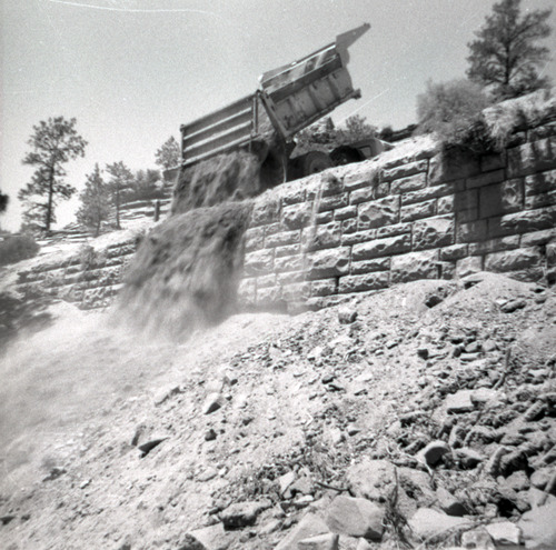 Dump truck dumping dirt over retaining wall during repairs of all along East Rim road.