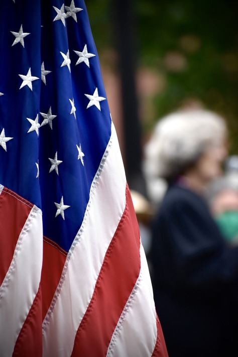 The American Flag hangs in the foreground with people in the background. 