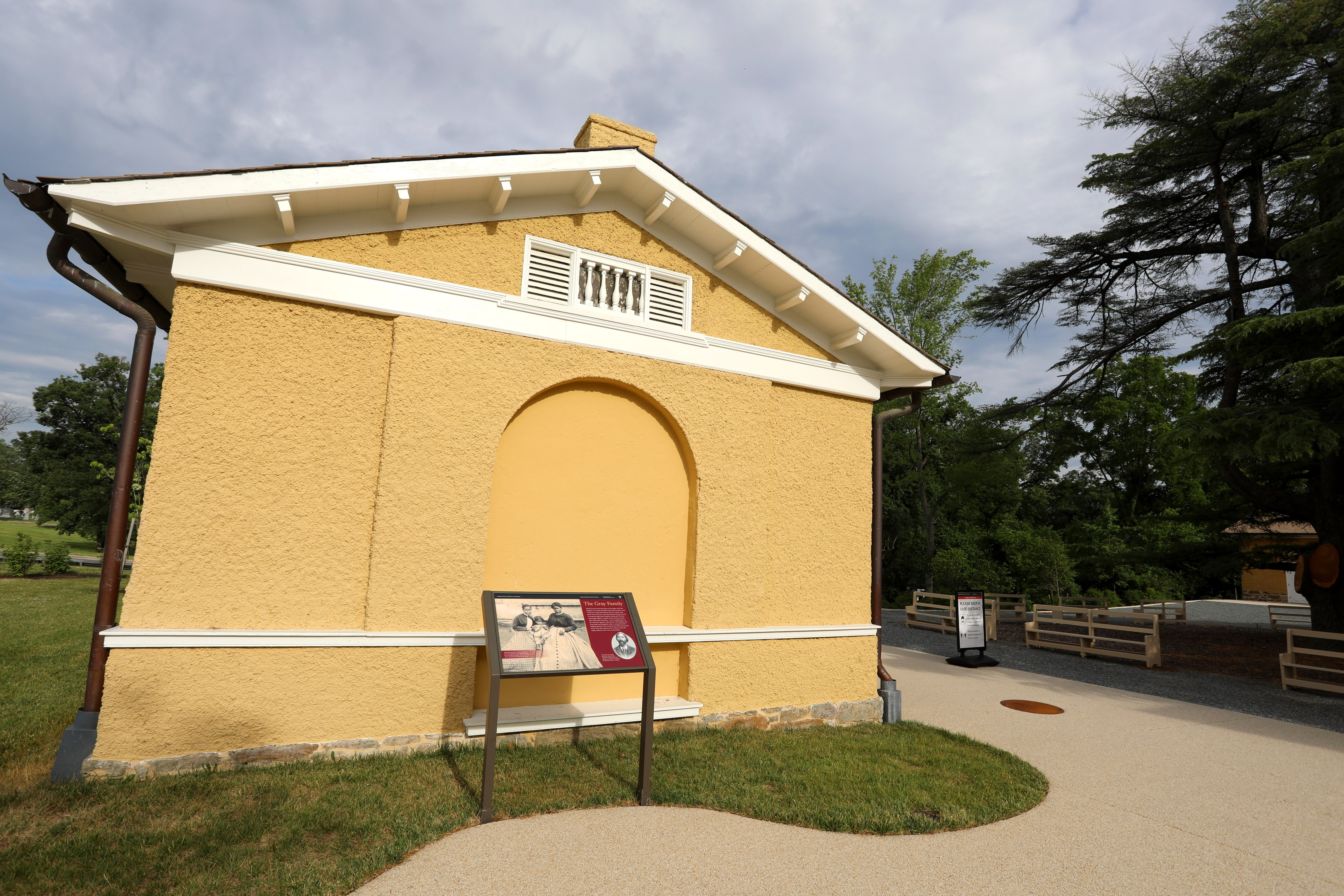 Exterior of the slave quarters at Arlington House, The Robert E. Lee Memorial.  A small yellow building with a wayside in front of it. 