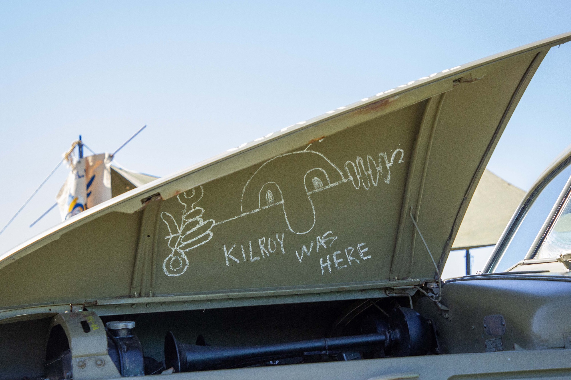 A green vehicle hood lifted up to show "Kilroy Was Here" written underneath