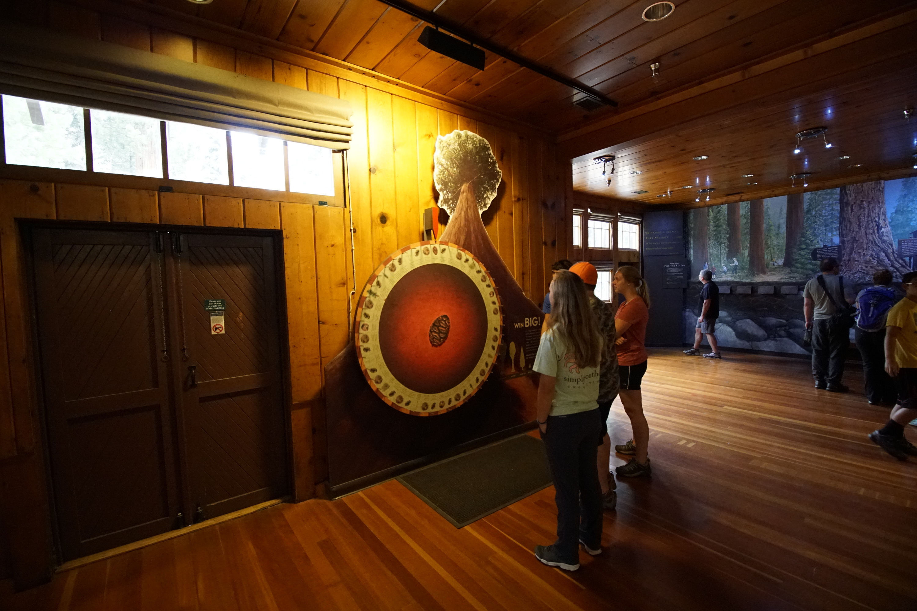 A wooden walled building interior. People can be seen looking at a big red spinning wheel with images on it 