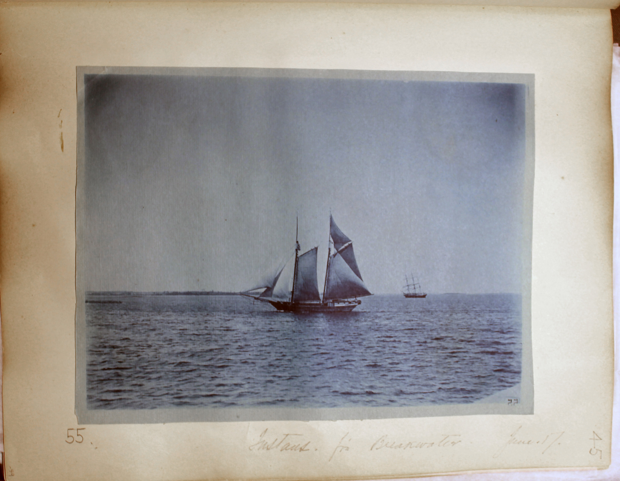 Blue toned photo of two-masted vessel sailing with three-masted vessel in right distance.