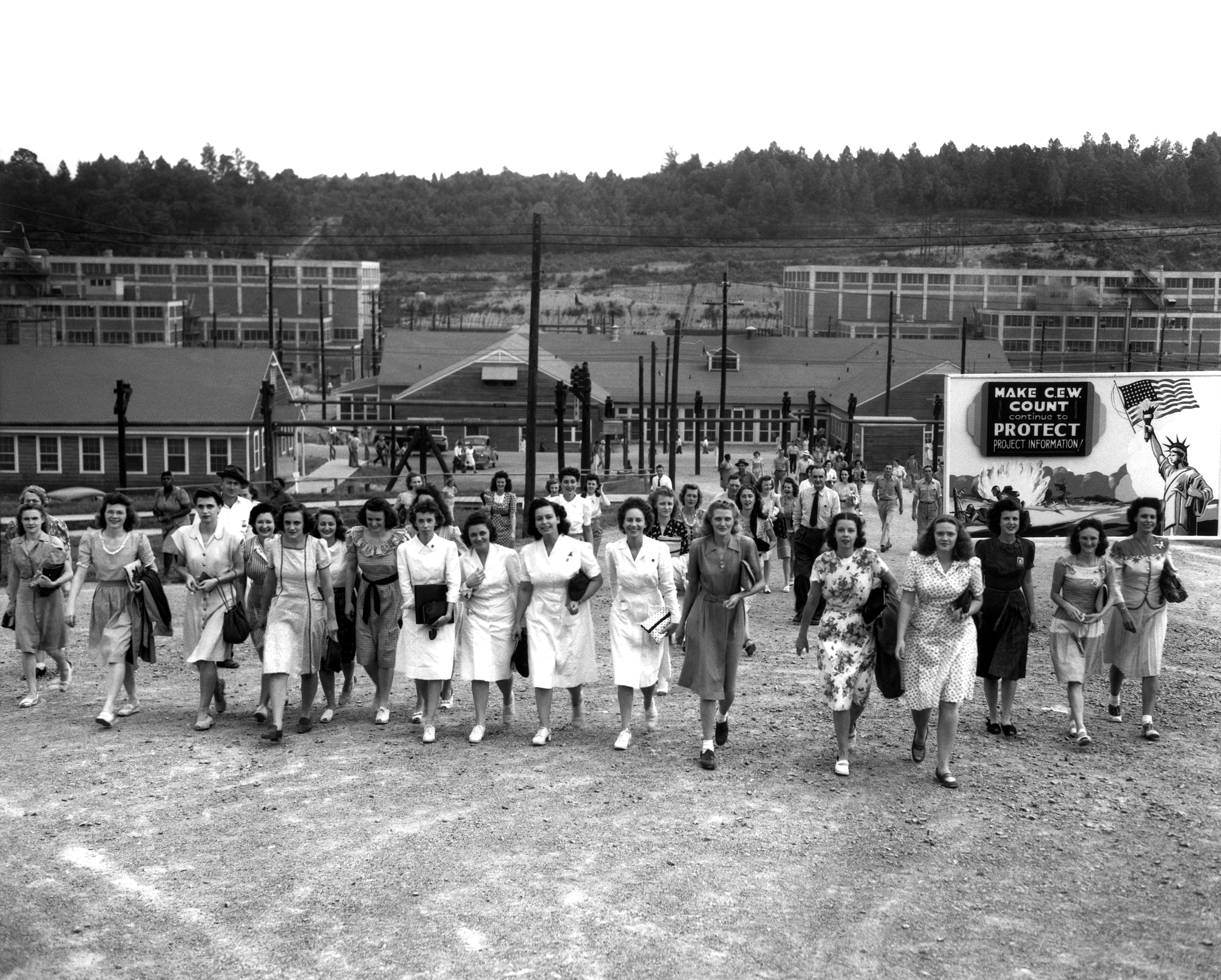 A group of women including several in nursing uniforms are walking from a gated area with multiple buildings.