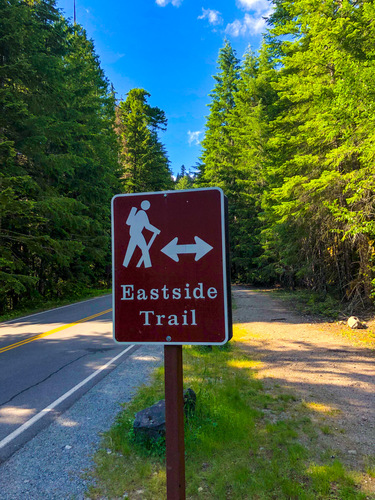 A brown sign stands on the side of the road and shows a hiker, a horizontal arrow and the words "Eastside Trail."
